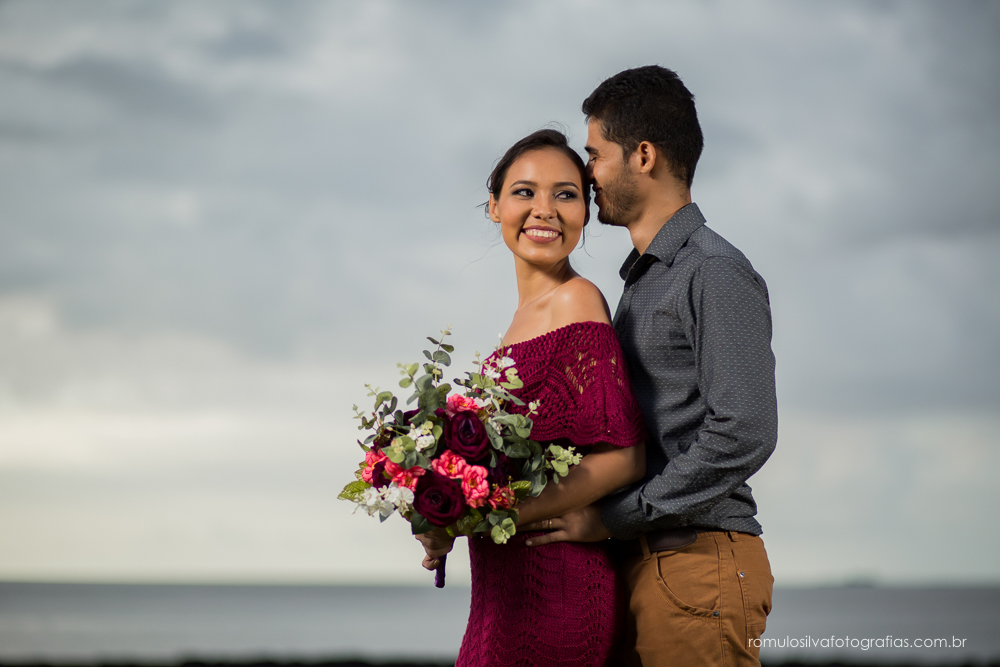 casal de noivos, Dulci e Glaisson, apaixonados, em uma pose linda, romântica, com um bouque em flores artificiais em uma paisagem linda e na beira da praia, no Chalé da Zuzu em Mosqueiro - PA