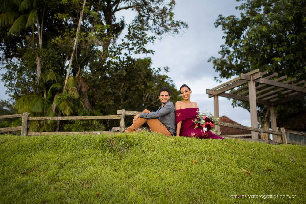casal de noivos, Dulci e Glaisson, apaixonados,sentados na grama, com um bouque em flores artificiais em uma paisagem linda e na beira da praia, no Chalé da Zuzu em Mosqueiro - PA