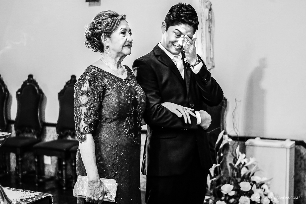 foto do noivo com a mãe enxugando as lágrimas durante a entrada da noiva 