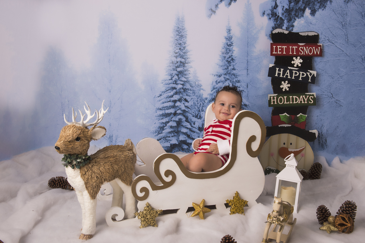 Ensaio fotográfico de Natal com roupas temáticas com crianças brincando na neve com trenó, rena e brinquedos polo norte