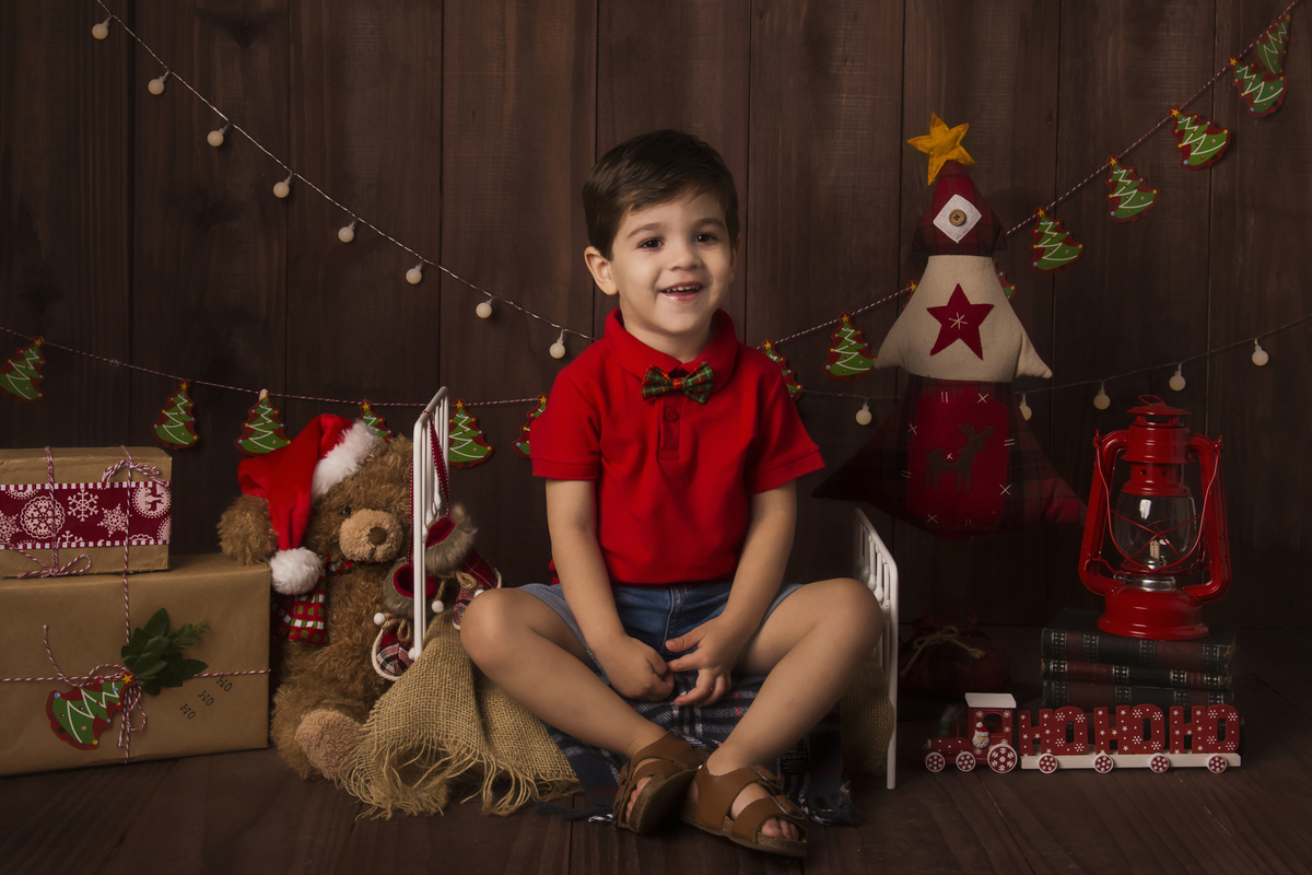 Ensaio fotográfico de Natal com roupas temáticas com crianças brincando no quartinho do Papai Noel com cama brinquedos arvore de natal presentes 