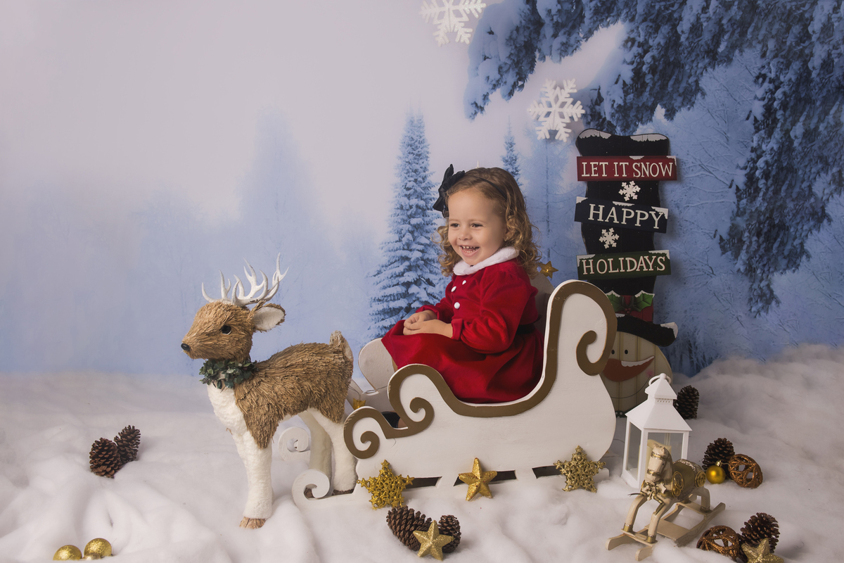Ensaio fotográfico de Natal com roupas temáticas com crianças brincando na neve com trenó, rena e brinquedos polo norte