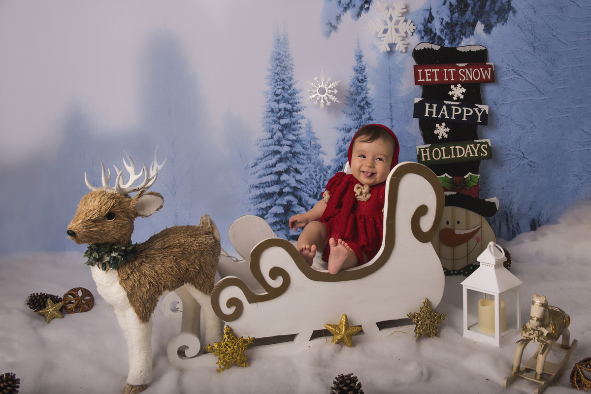 Ensaio fotográfico de Natal com roupas temáticas com crianças brincando na neve com trenó, rena e brinquedos polo norte
