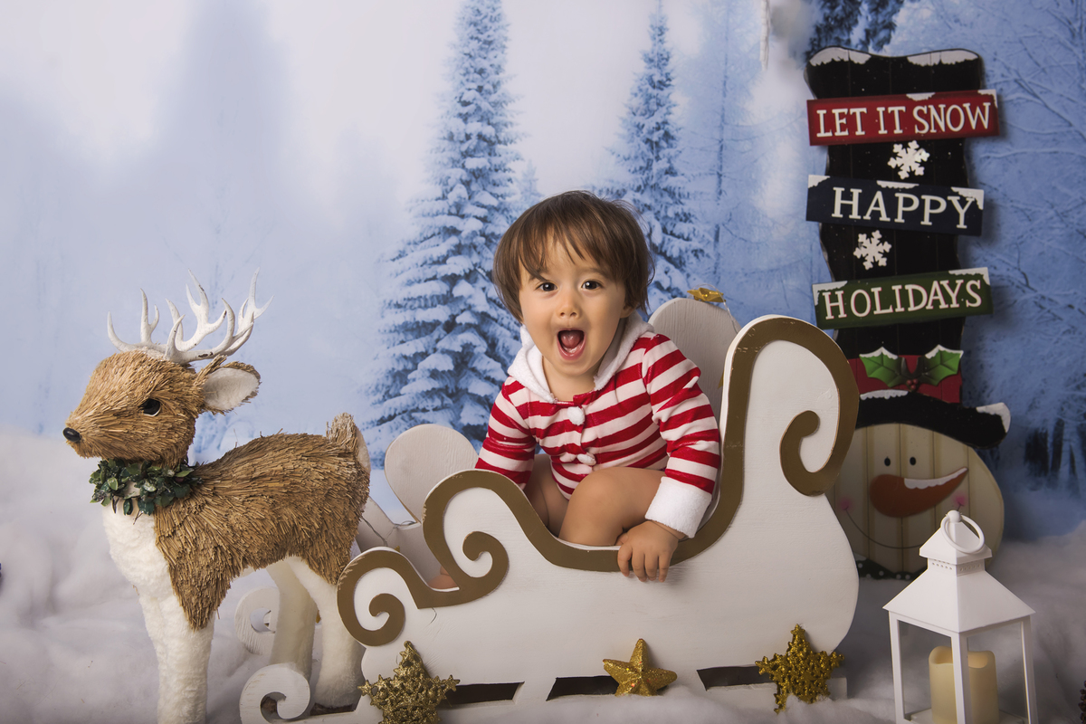 Ensaio fotográfico de Natal com roupas temáticas com crianças brincando na neve com trenó, rena e brinquedos polo norte