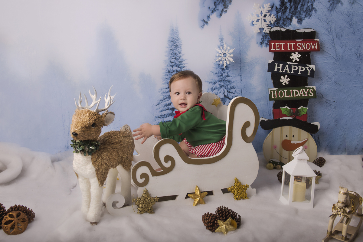 Ensaio fotográfico de Natal com roupas temáticas com crianças brincando na neve com trenó, rena e brinquedos polo norte