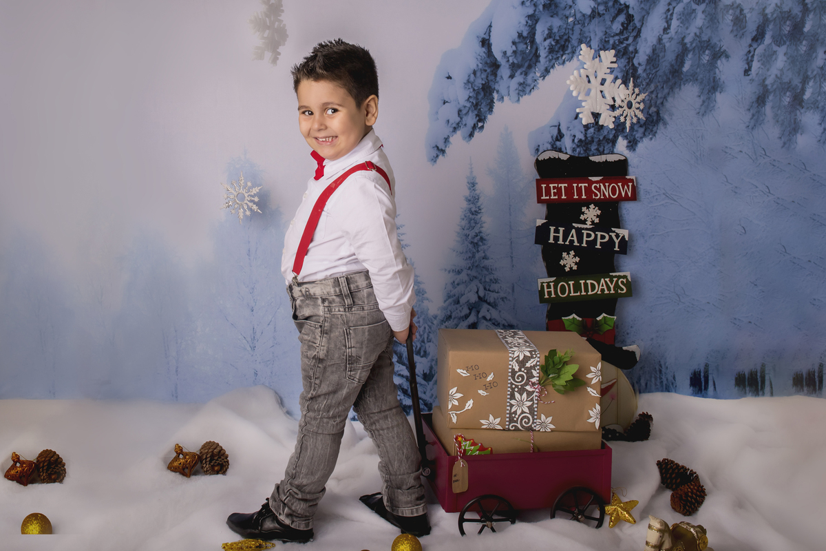 Ensaio fotográfico de Natal com roupas temáticas com crianças brincando na neve com trenó, rena e brinquedos polo norte