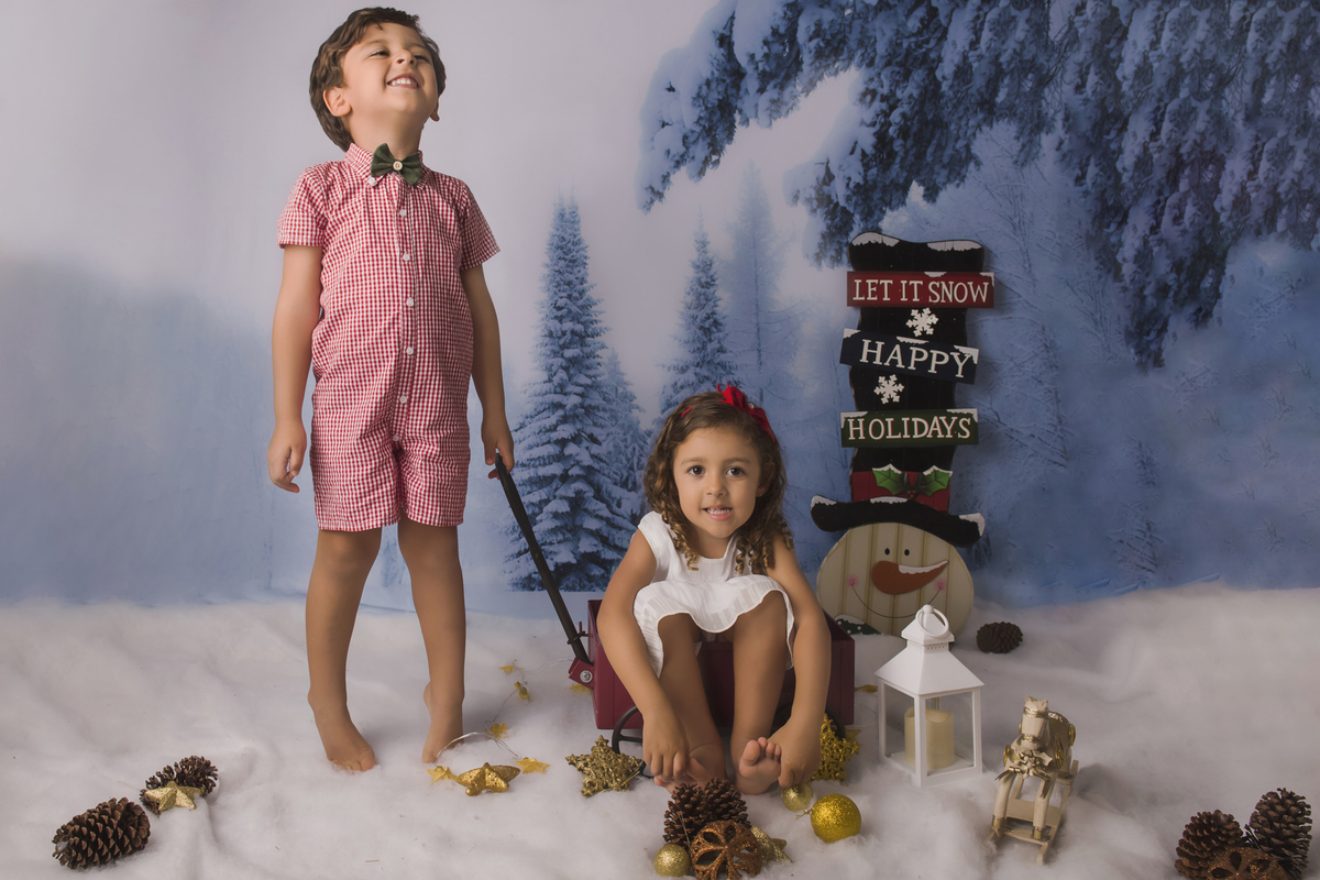 Ensaio fotográfico de Natal com roupas temáticas com crianças brincando na neve com trenó, rena e brinquedos polo norte