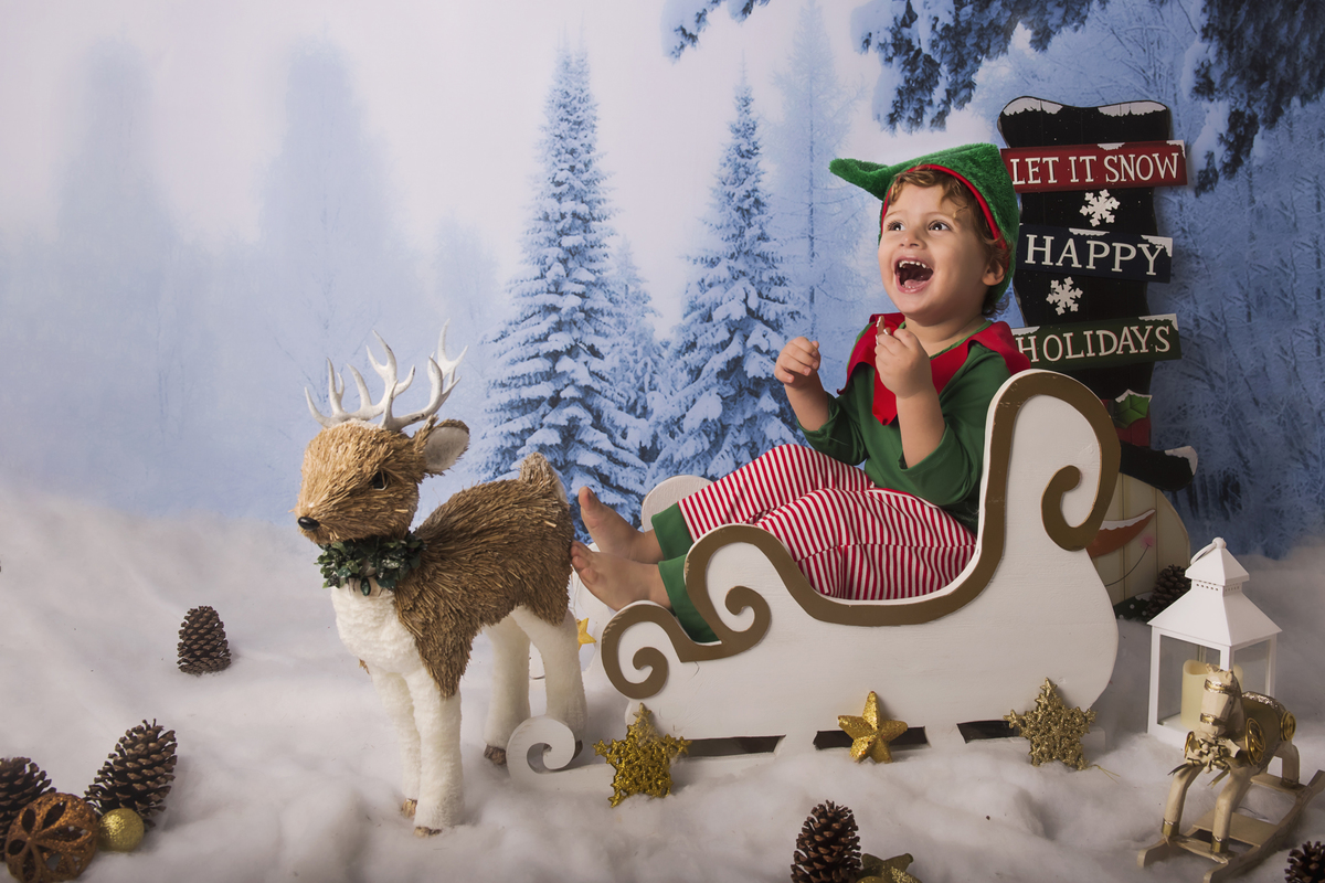 Ensaio fotográfico de Natal com roupas temáticas com crianças brincando na neve com trenó, rena e brinquedos polo norte