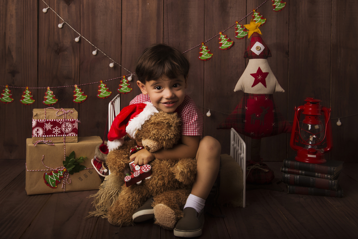 Ensaio fotográfico de Natal com roupas temáticas com crianças brincando no quartinho do Papai Noel com cama brinquedos arvore de natal presentes 