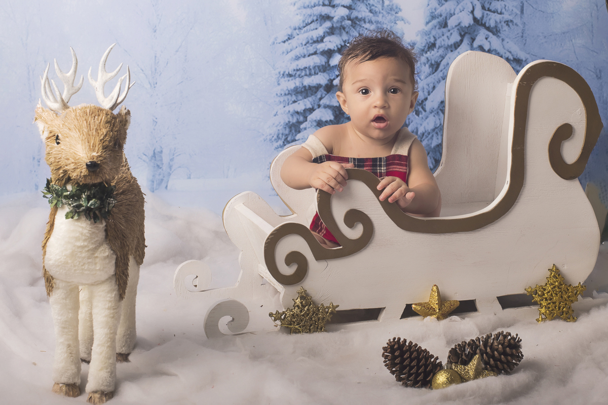 Ensaio fotográfico de Natal com roupas temáticas com crianças brincando na neve com trenó, rena e brinquedos polo norte