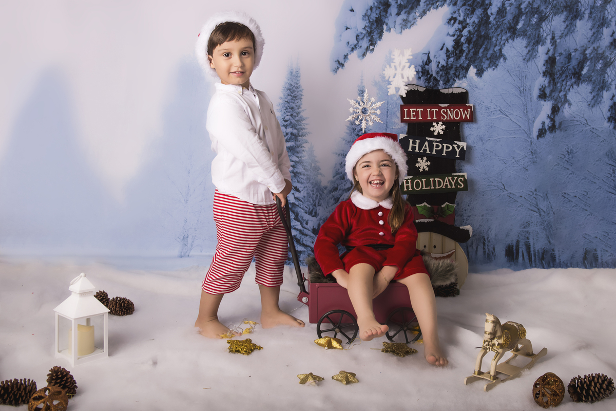 Ensaio fotográfico de Natal com roupas temáticas com crianças brincando na neve com trenó, rena e brinquedos polo norte