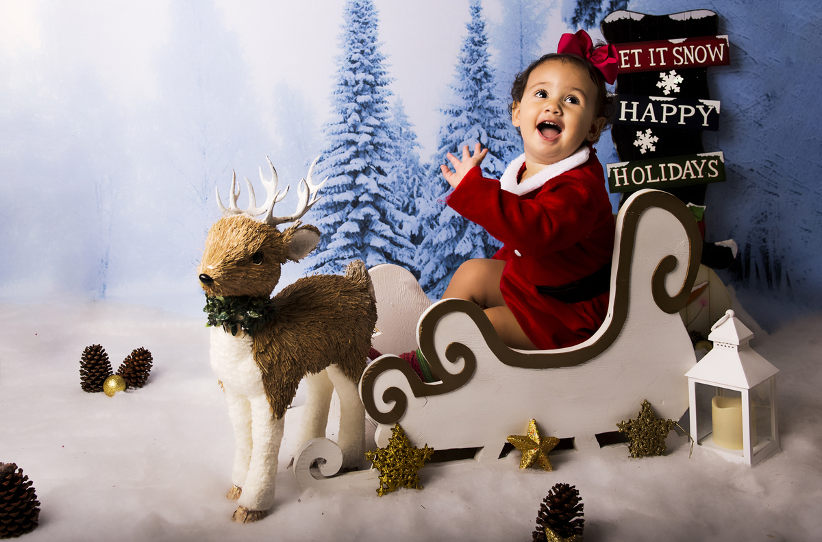 Ensaio fotográfico de Natal com roupas temáticas com crianças brincando na neve com trenó, rena e brinquedos polo norte