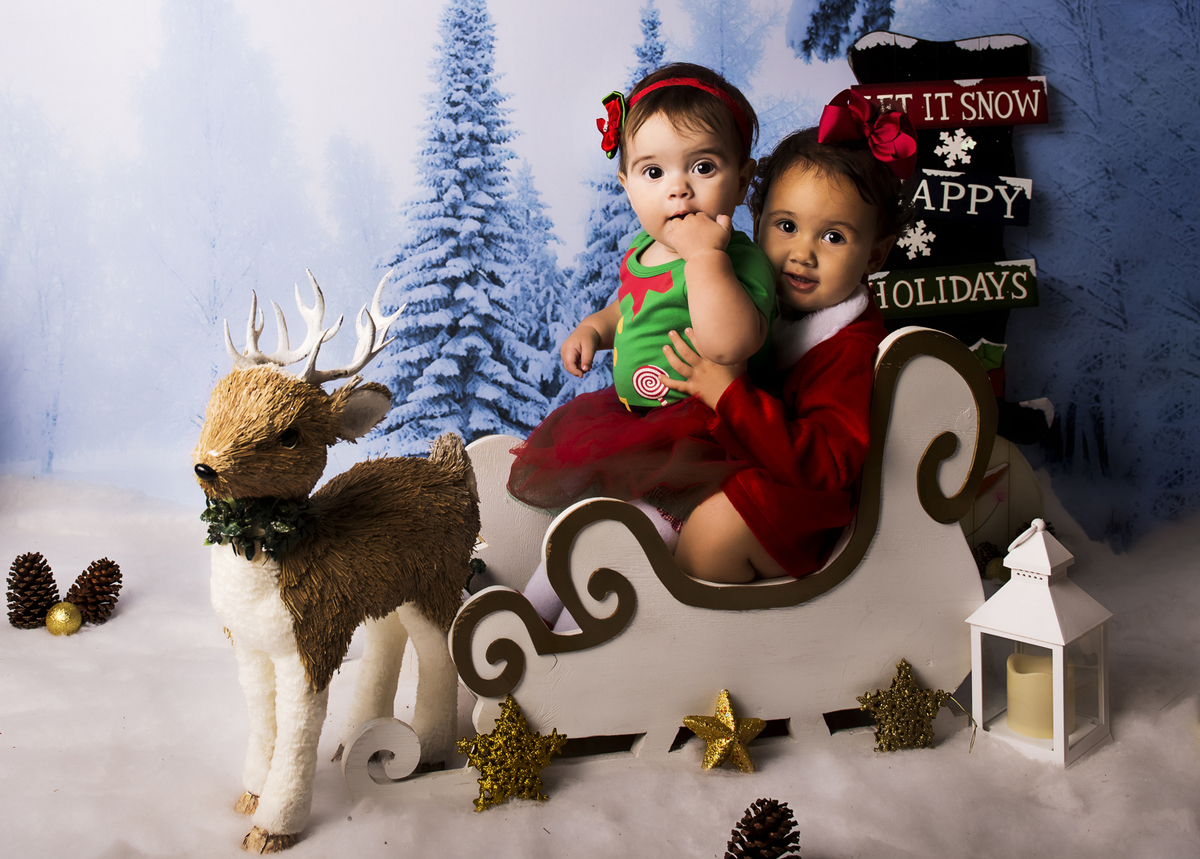 Ensaio fotográfico de Natal com roupas temáticas com crianças brincando na neve com trenó, rena e brinquedos polo norte