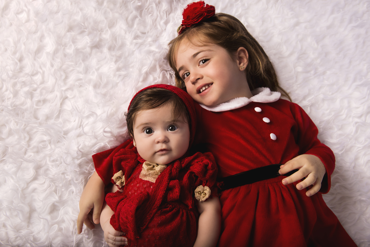 Ensaio fotográfico de Natal com roupas temáticas com crianças brincando na neve com trenó, rena e brinquedos polo norte