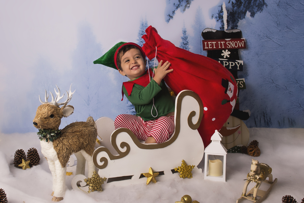 Ensaio fotográfico de Natal com roupas temáticas com crianças brincando na neve com trenó, rena e brinquedos polo norte