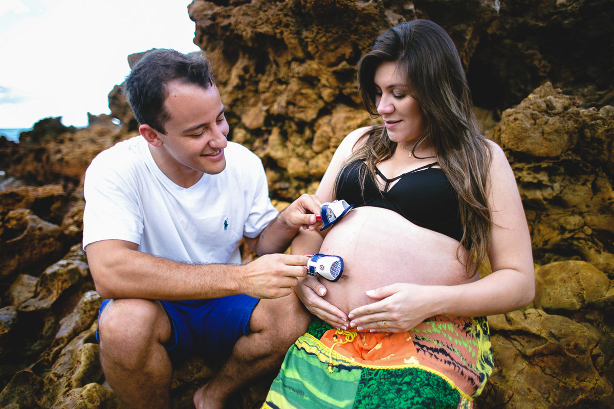 pai brincando com sapatinho de bebê e esposa grávida sorrindo e pegando na barriga