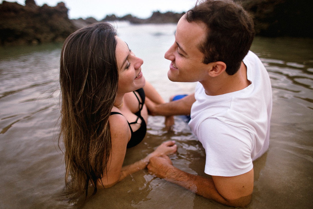 casal se olhando deitados na água na beira do mar