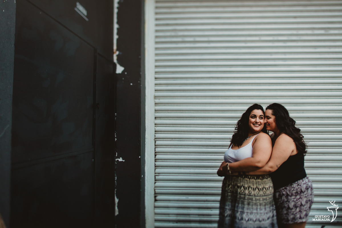 mulher abraça a namorada por trás em frente a portão de uma loja