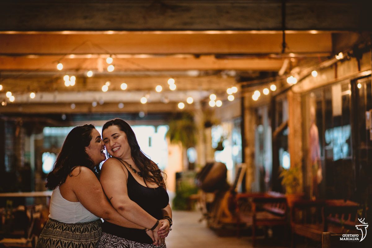 mulher abraça a namorada por trás e dá um cheiro no seu pescoco