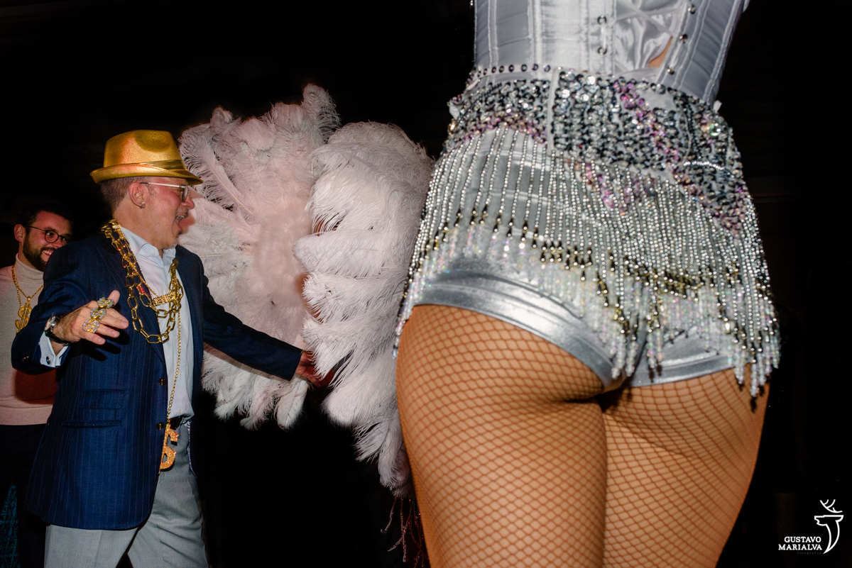 dançarina usando fantasia prateada e segurando penas dança enquanto ao fundo homem usando chapéu dormido dança animado