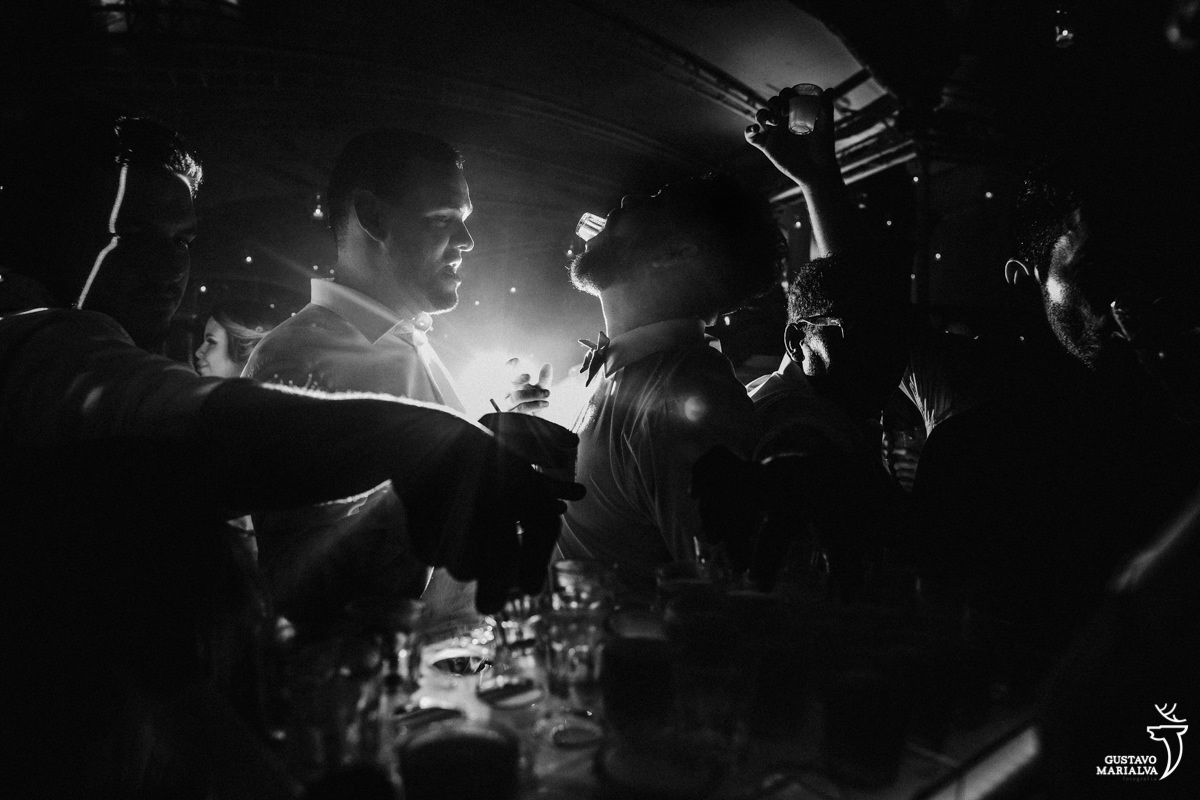 homem enfia copo de shot na boca e vira a bebida com luz do flash iluminando o fundo