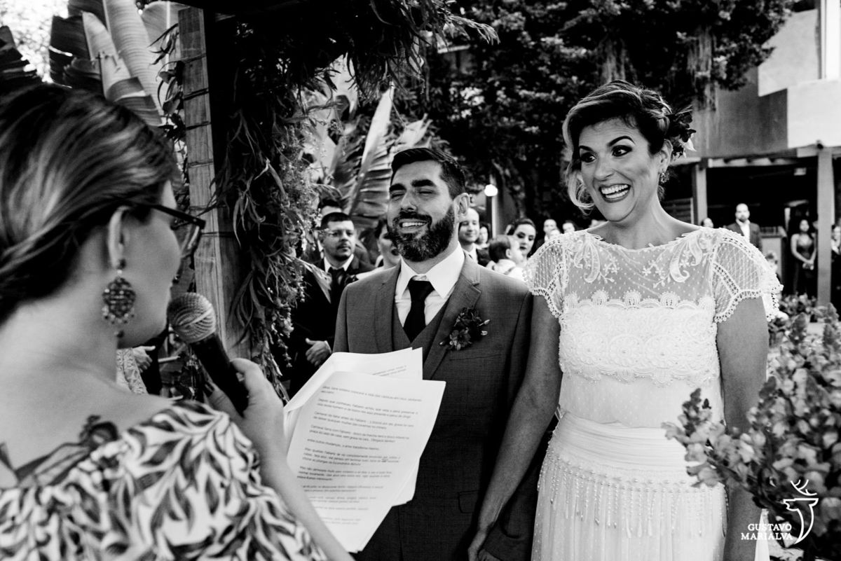 noivos de mãos dadas sorriem e observam a celebrante 