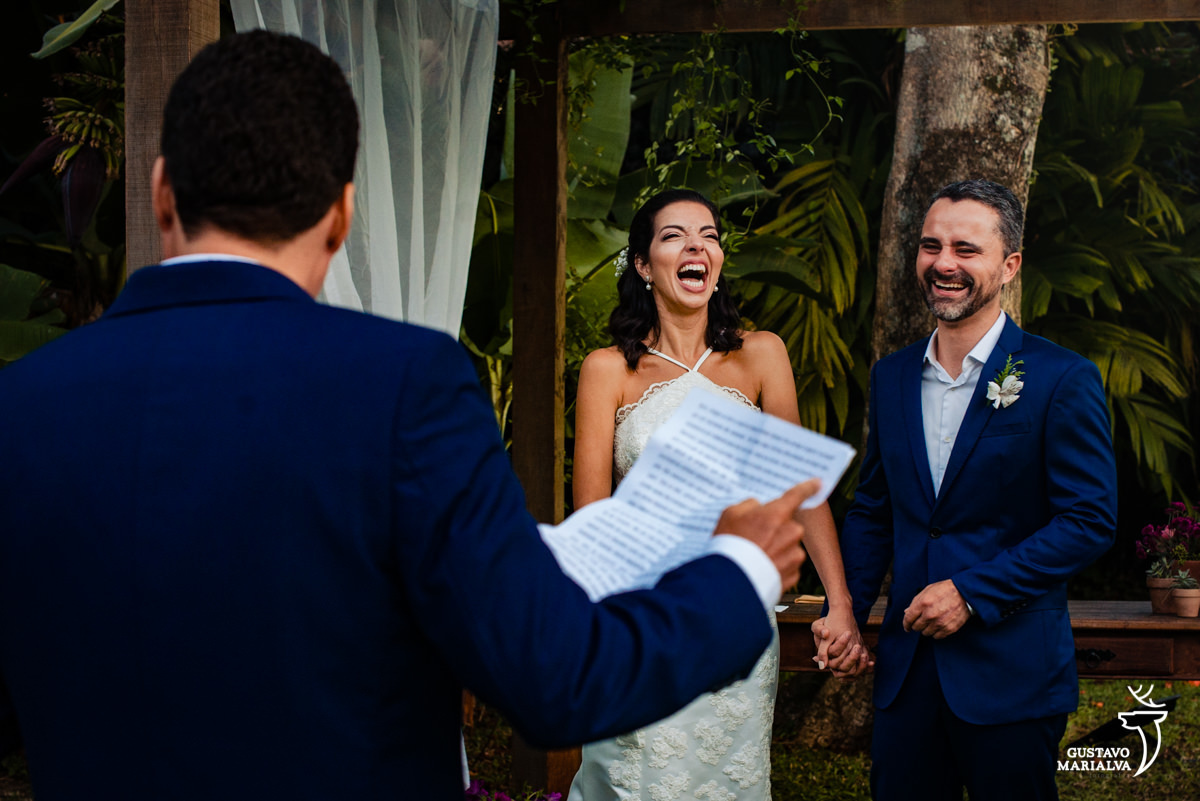 noivos de mãos dadas sorriem com discurso de amigo que usa terno azul
