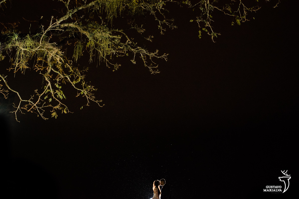 Casal se abraça iluminados por luz de flash e pingos de chuva detalhados no céu