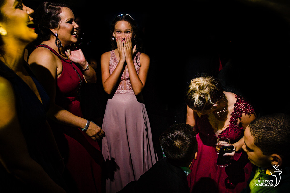 menina usando vestido rosa coloca as mãos no rosto e faz cara de espanto enquanto mulher usando vestido vinho rebola até o chão