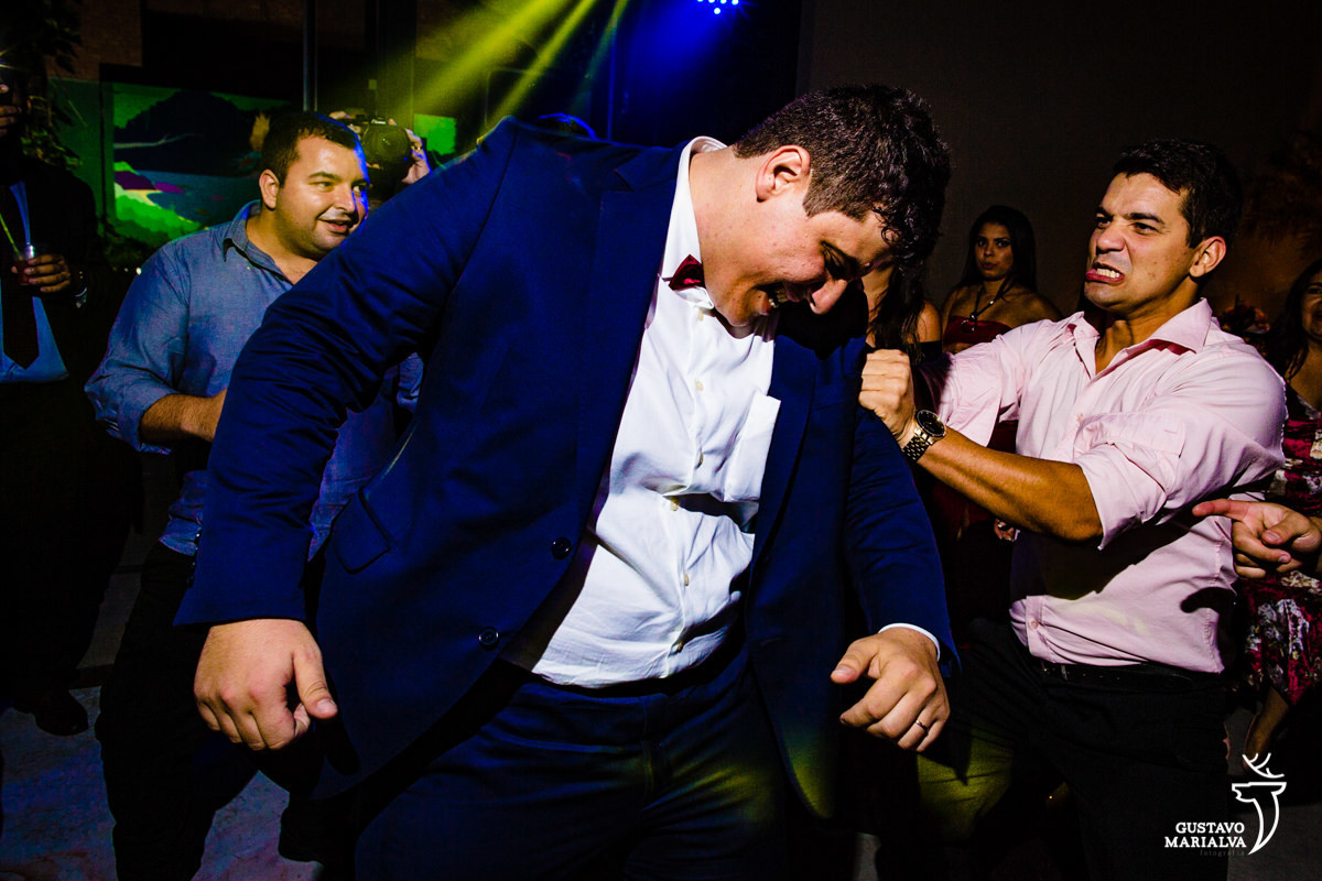 homem usando camisa rosa tenta arrancar terno azul do noivo que sorri