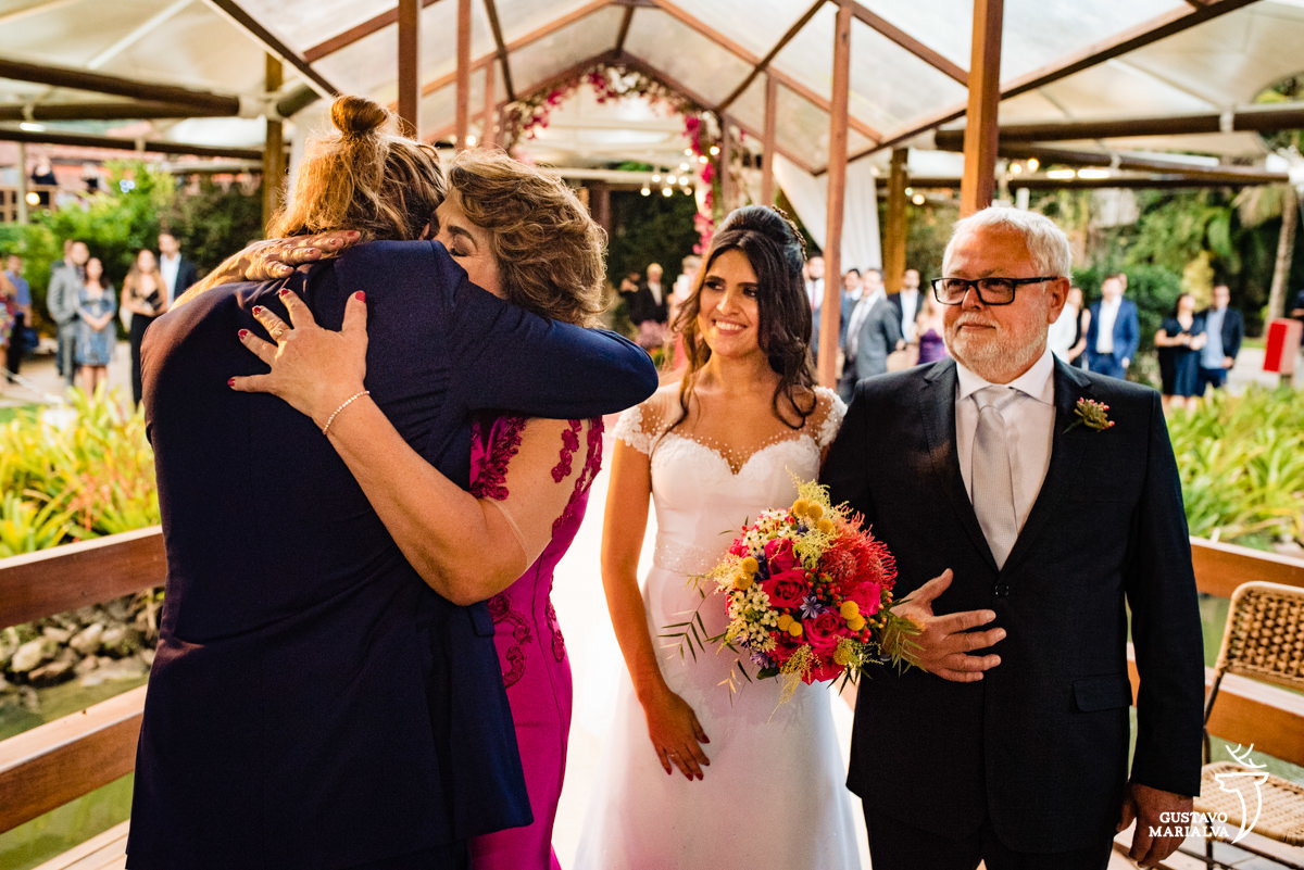 mãe da noiva abraça noivo emocionado enquanto é observado pela noiva e pelo pai da noiva