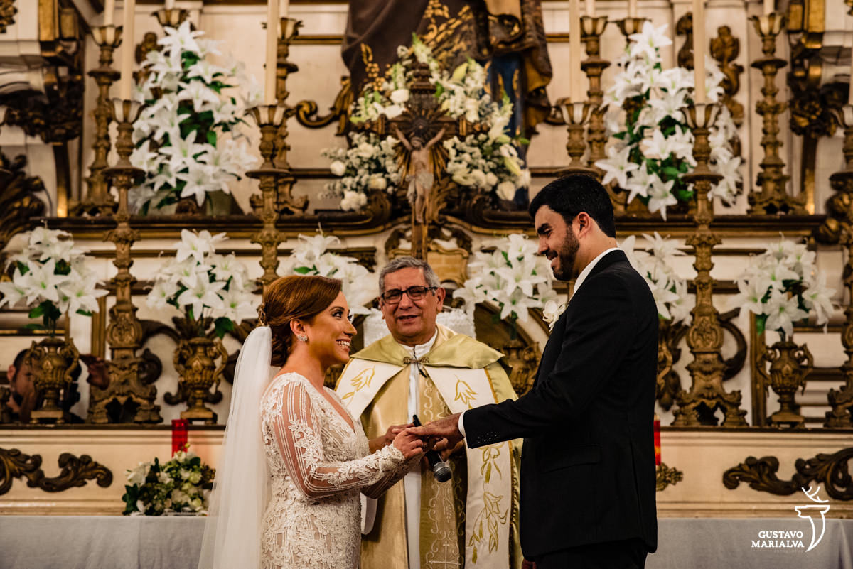 noiva emocionada coloca aliança da mão do noivo que sorri