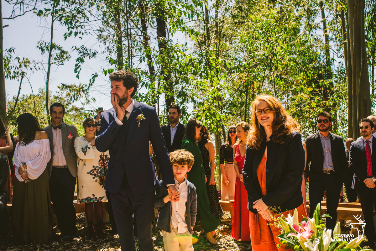 noivo usando terno azul de mãos dadas com o vilho coloca a mão no rosto emocionado