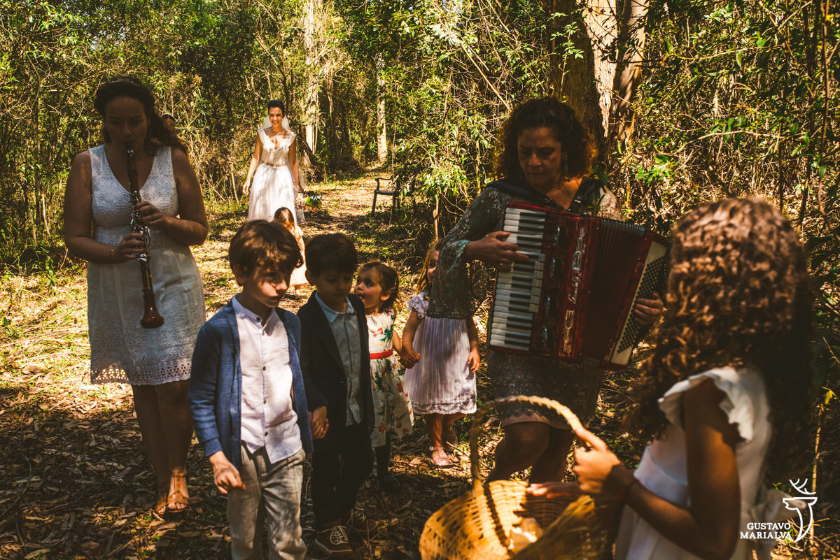 noiva anda na floresta enquanto amigas tocando flauta e sanfona andam na frente acompanhas de pajens