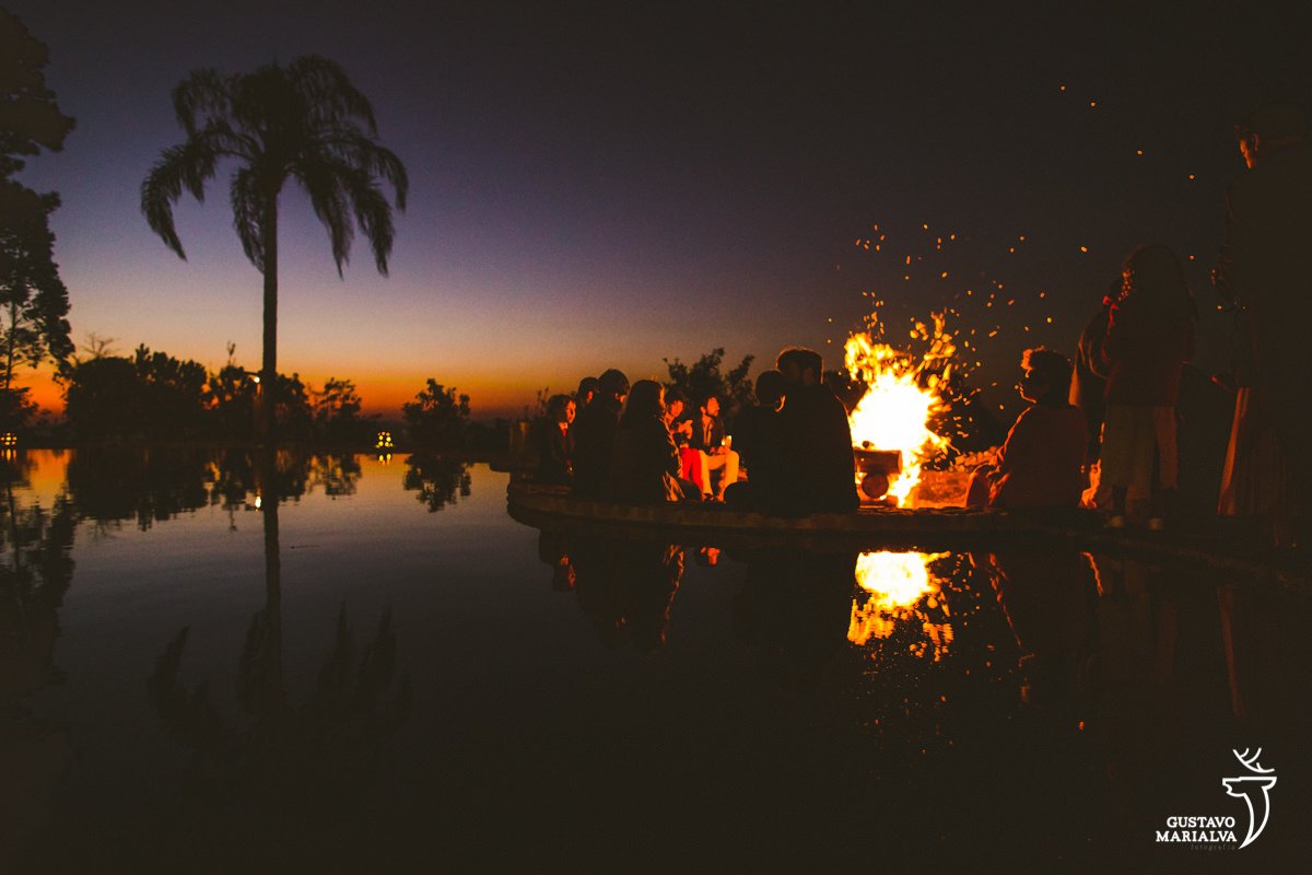 pessoas sentam envolta de fogueira enquanto observam o por do sol