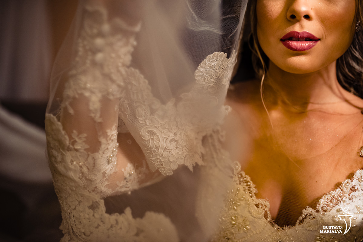 noiva segura o véu de noiva em frente ao rosto e mostra a boca com batom rosa