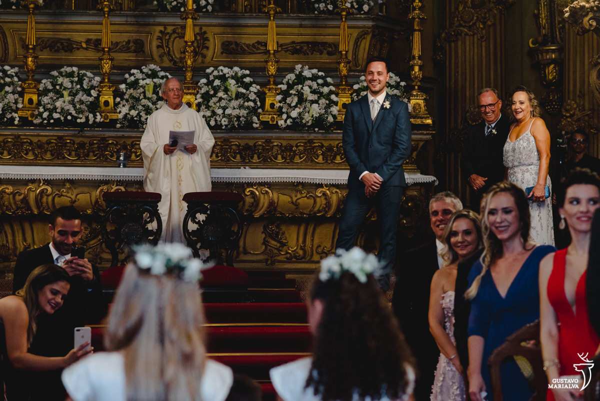 noivo usando terno azul sorri ao ver os pajens e daminhas entrarem