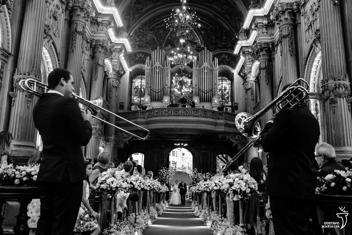 noiva entra na igreja durante a cerimônia de casamento enquanto homens tocam instrumento de sopro