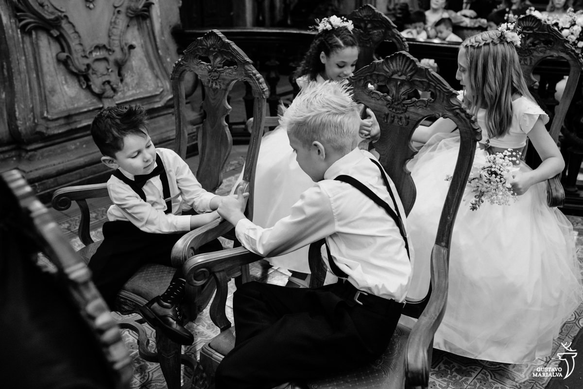 pajens de camisa branca e suspensório preto brincam durante a cerimônia de casamento 