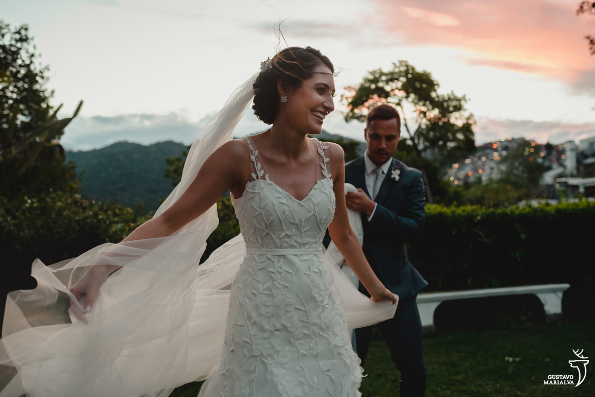 noiva sorri ao rodar com o véu enquanto noivo usando terno azul segura o véu
