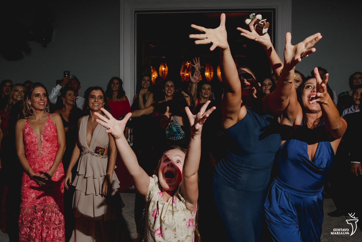 menina faz cara de assustada ao tentar pegar o buquê enquanto mulheres usando vestido azul pulam para pegar