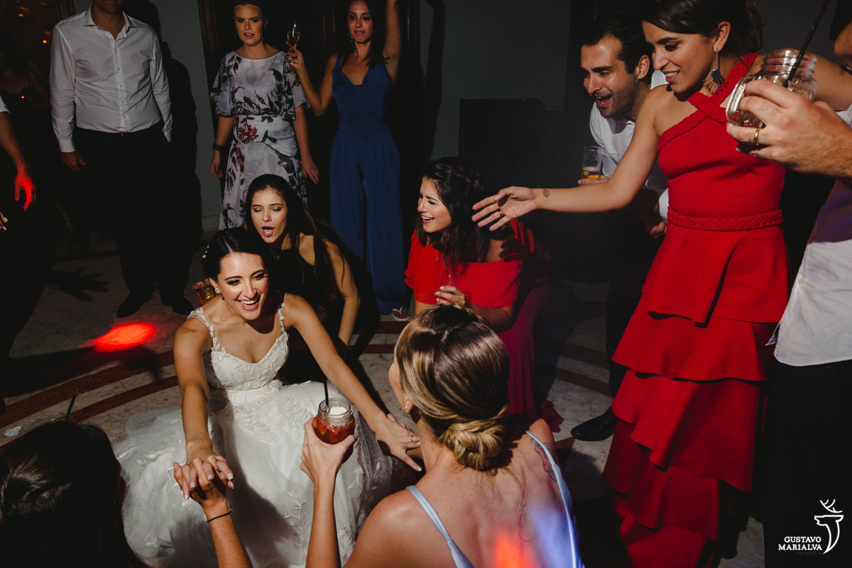 noiva dança com amigas descendo até o chão enquanto amiga usando vestido vermelho sorri