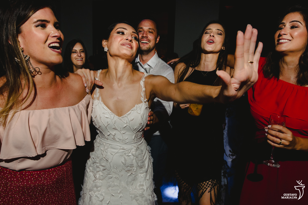 noiva dança abraçada com amiga que usa vestido rosa e vermelho enquanto amigas sorriem
