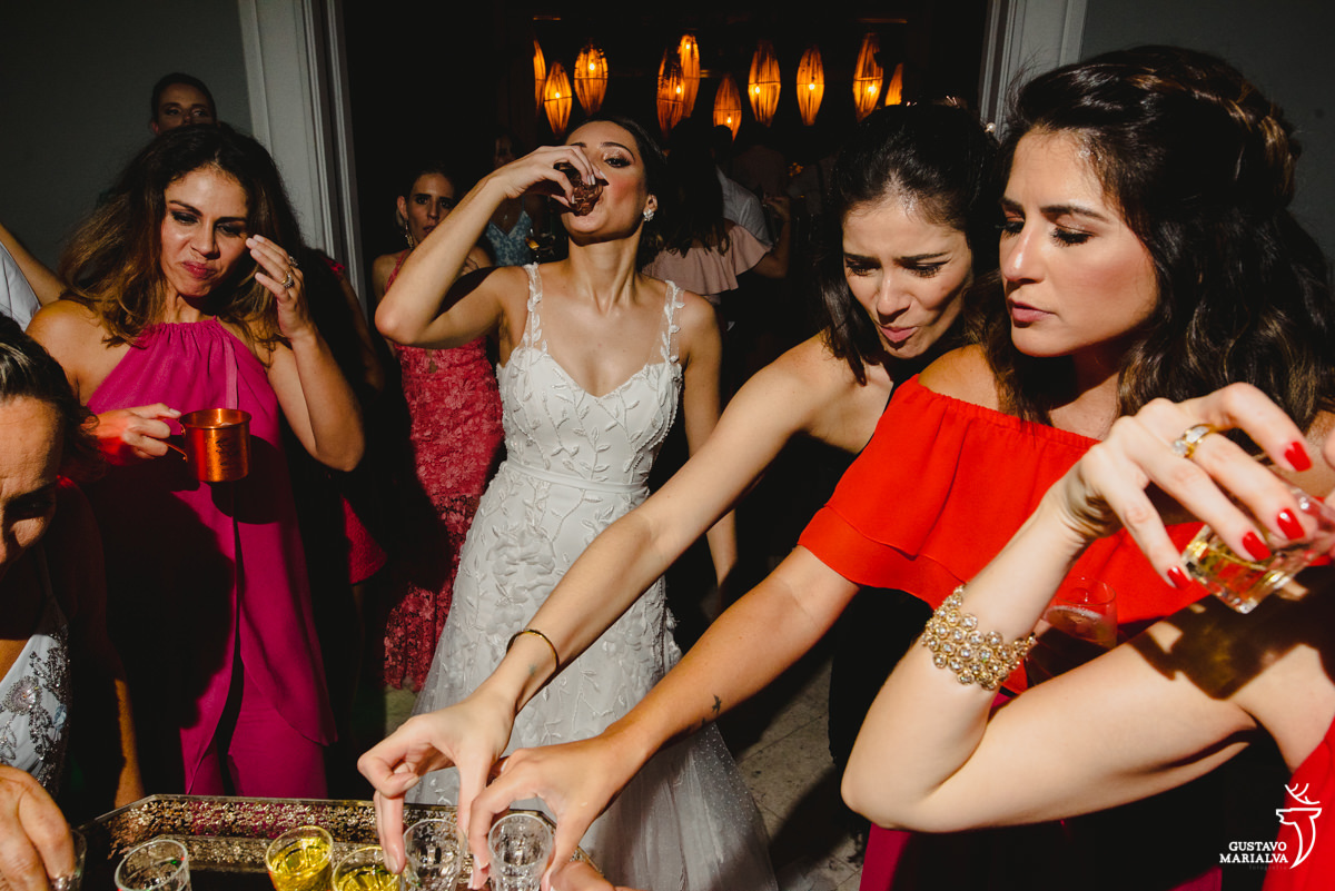 noiva toma shot de cachaça enquanto amiga de vestido vermelho acomapnha