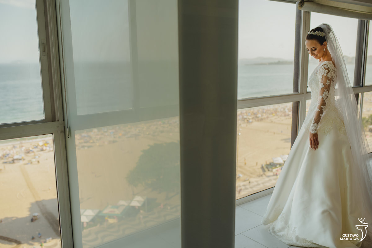 noiva usando vestido carol hungria posa para foto na sala do seu apartamento com a praia de copacabana ao fundo