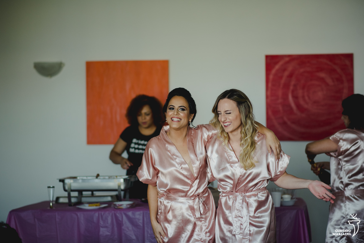 noiva usando robe rosa abraça madrinha loira que sorri