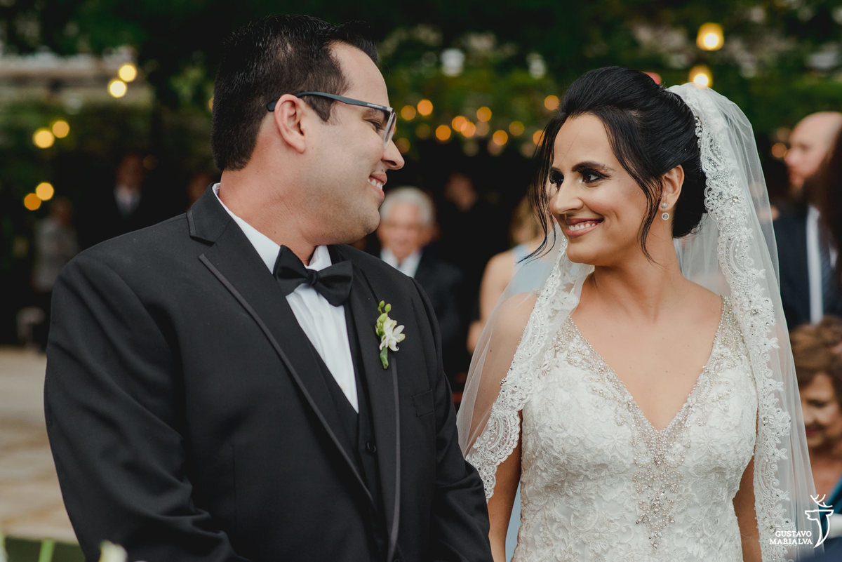 noivo usando smoking olha sorridente para a noiva durante a cerimônia de casamento