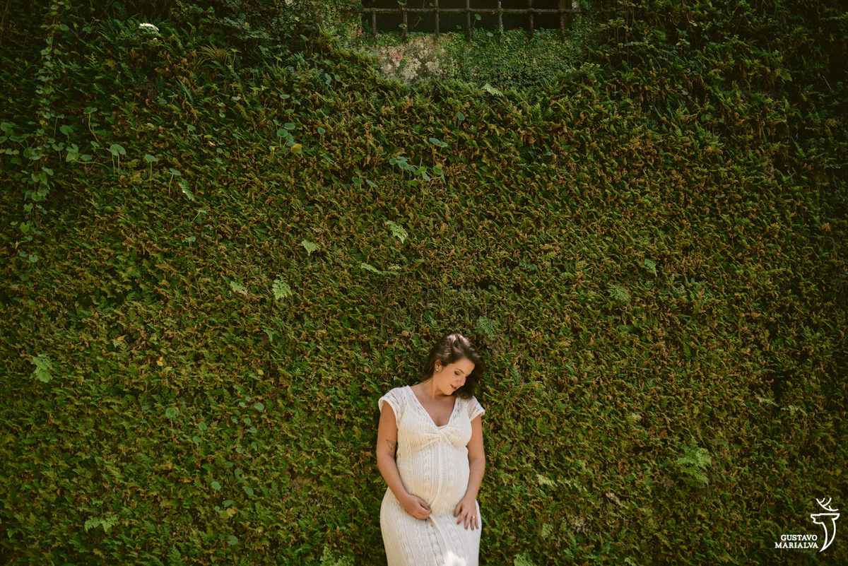 mulher grávida posa em frente a muro verde de plantas