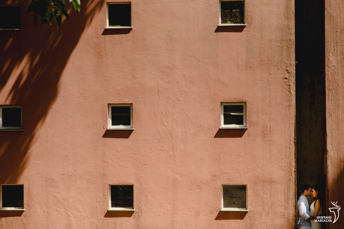 casal se abraça em vão de prédio com a parede de cor terra