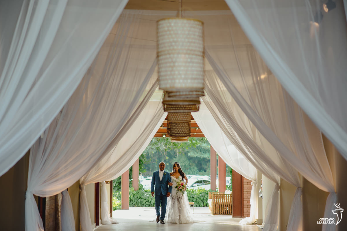 pai da noiva usando terno azul abraça a noiva em corredor com luminárias no galeria jardim